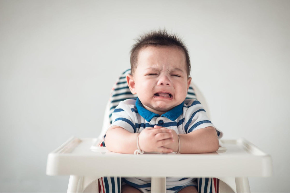 Niño pequeño sentado en su silla de comer rechazando la comida